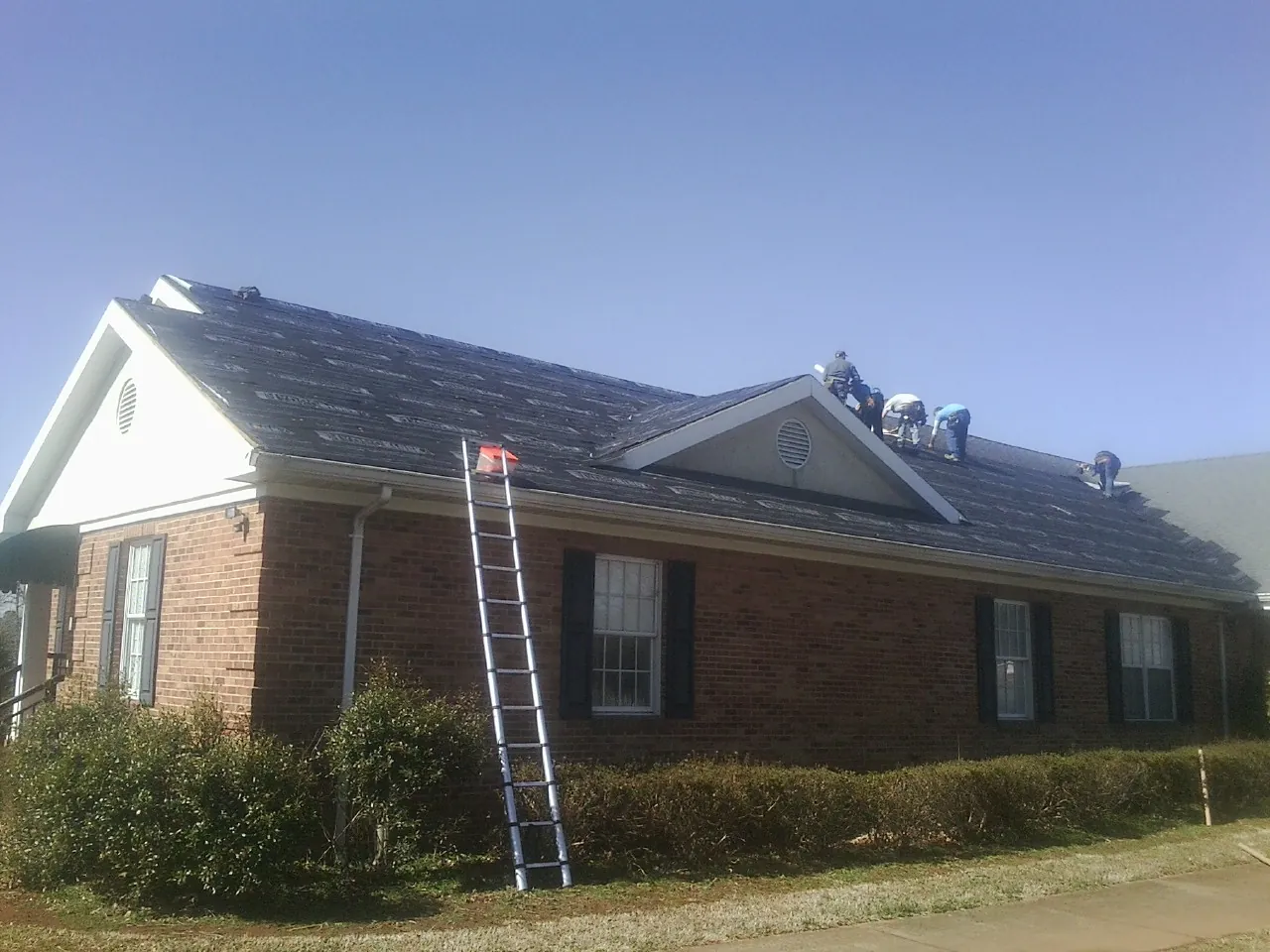Crew tearing shingles off a brick ranch roof with a ladder set — Emergency Roof Repair work by our crew in Highlands