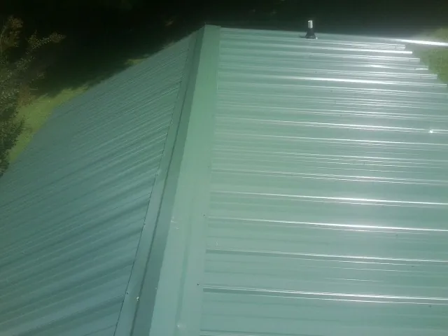 New green metal panels meeting at the ridge of a roof — Flat Roof Repair work by our crew in Highlands