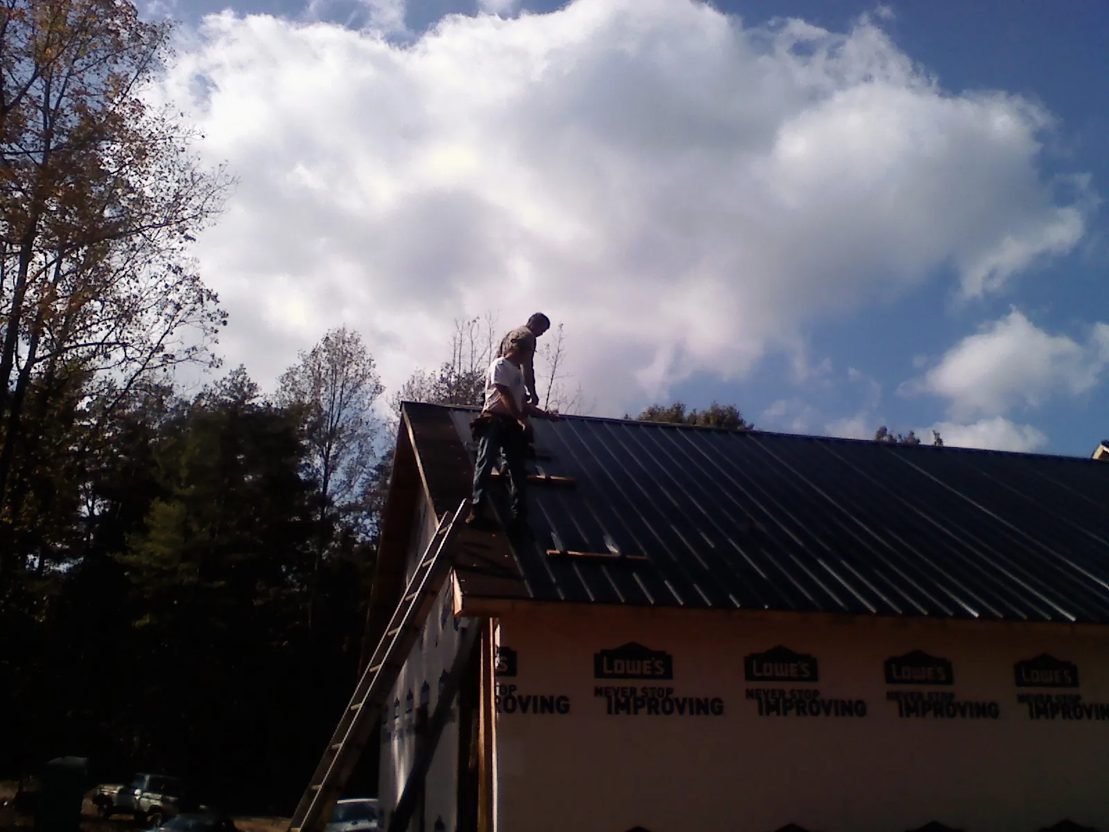 Roofer fastening dark metal panels high against a cloudy sky, from a Roof Inspection job in Highlands